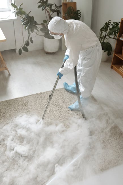 Close-up of a vacuum cleaner with a transparent dust collection chamber filled with dust and debris, connected to a flexible, patterned hose attached to a floor attachment, positioned on a pink carpet